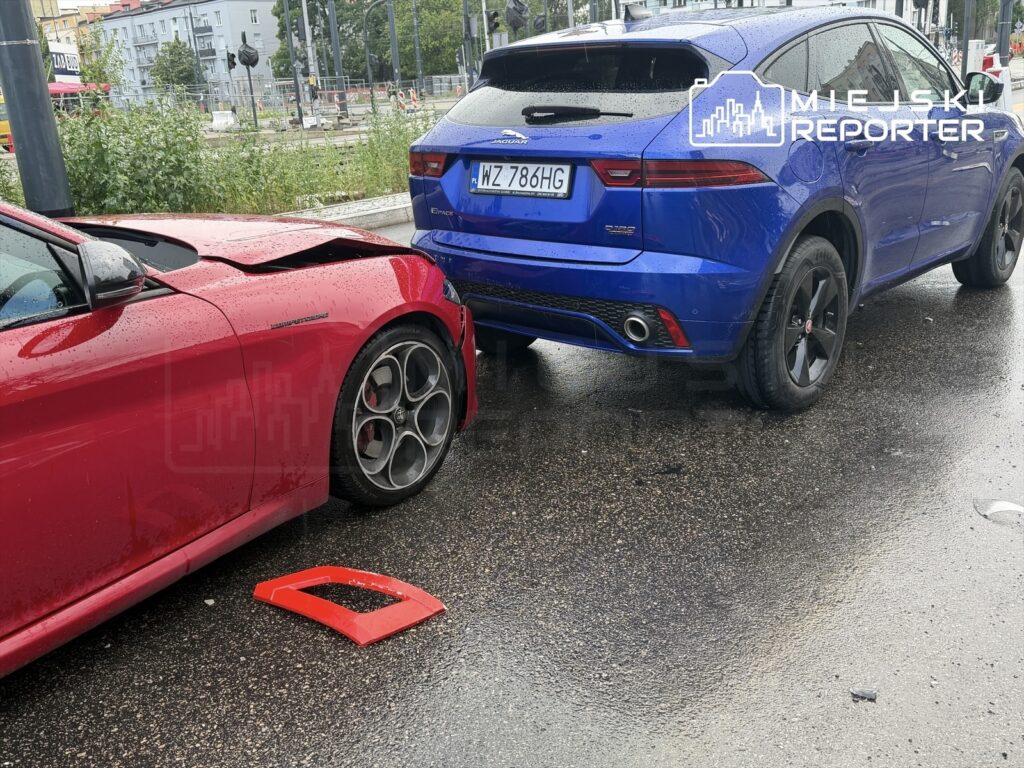 Czerwony samochód osobowy z uszkodzeniem tyłu stoi obok niebieskiego SUV-a na mokrej nawierzchni.
