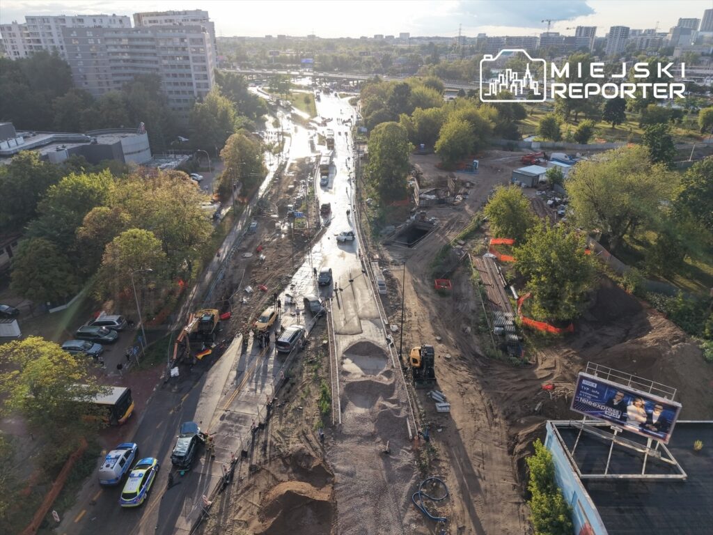 Roboty drogowe trwają na ulicy, obok wykopów i maszyn budowlanych, w otoczeniu budynków mieszkalnych.