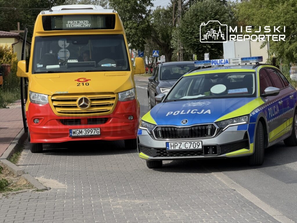 Autobus w kolorze czerwono-żółtym zatrzymany na poboczu, obok nieoznakowany radiowóz policyjny.