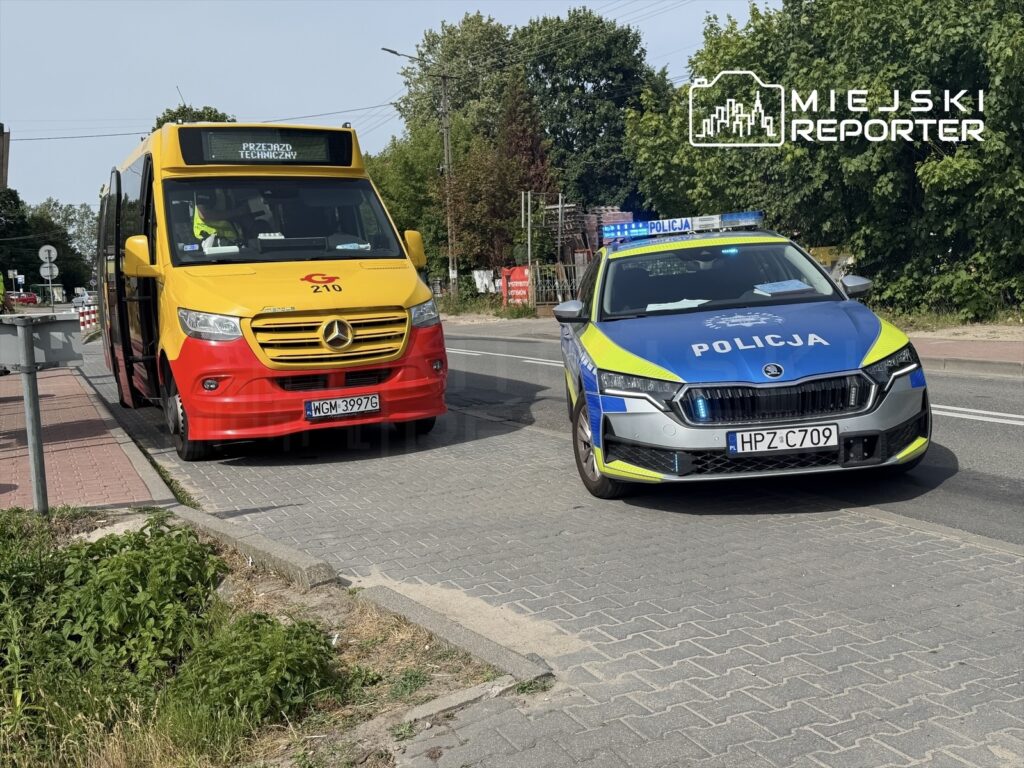 Autobus w kolorze żółto-czerwonym zatrzymany na przystanku, obok radiowóz policji z włączonymi sygnałami świetlnymi.
