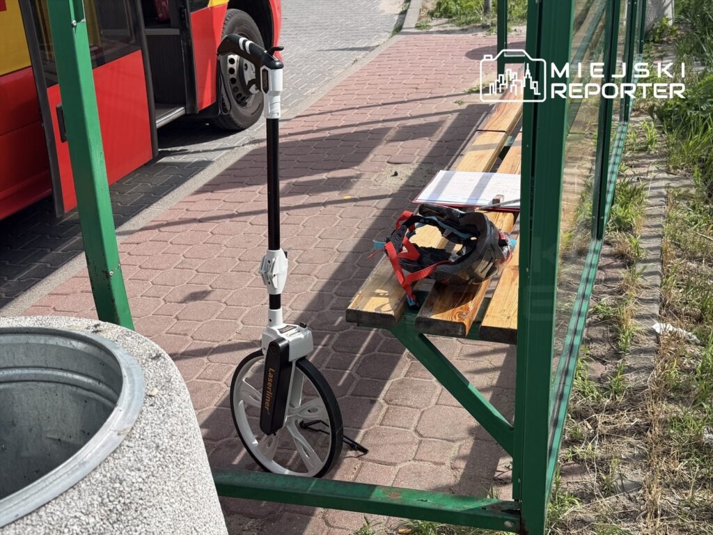 Skuter elektryczny stoi przy przystanku autobusowym obok drewnianej ławki i kasku ochronnego.