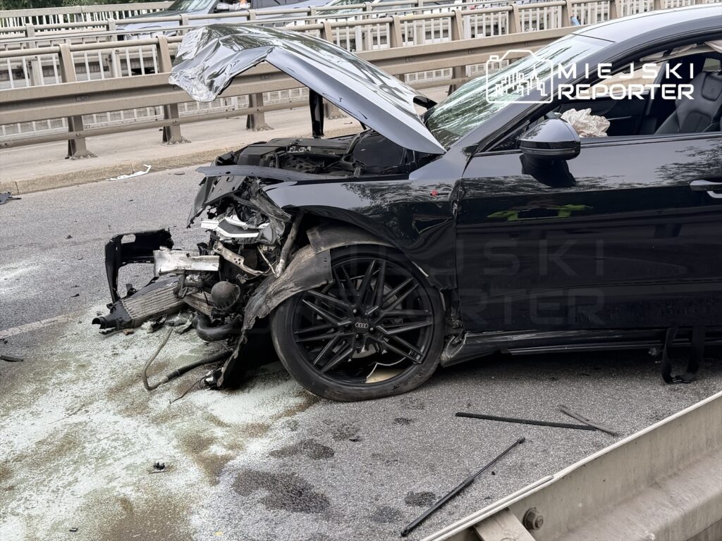 Zniszczony samochód osobowy z uszkodzonym przodem leży na jezdni, obok widać porozrzucane fragmenty.
