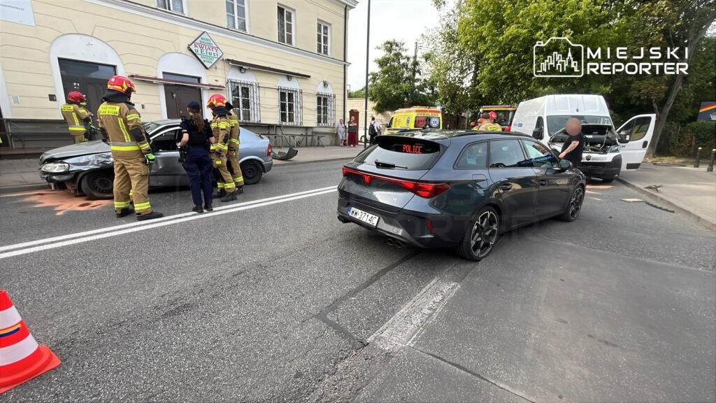 Strażacy oraz policjant pomagają poszkodowanym w wypadku drogowym na ulicy przy cmentarzu, gdzie zderzyły się dwa samochody.