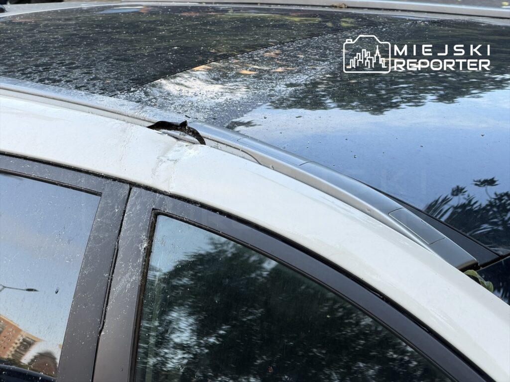 Uszkodzona karoseria samochodu osobowego z widocznymi śladami po silnym wietrze, parkowanego na ulicy.