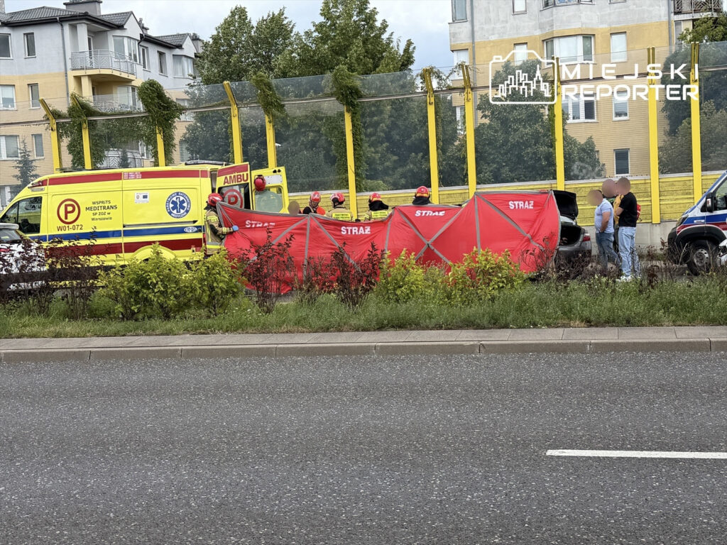 Zespół ratunkowy w czerwonych strojach ustawia namiot, podczas gdy karetka stoi obok wzdłuż ruchliwej drogi.