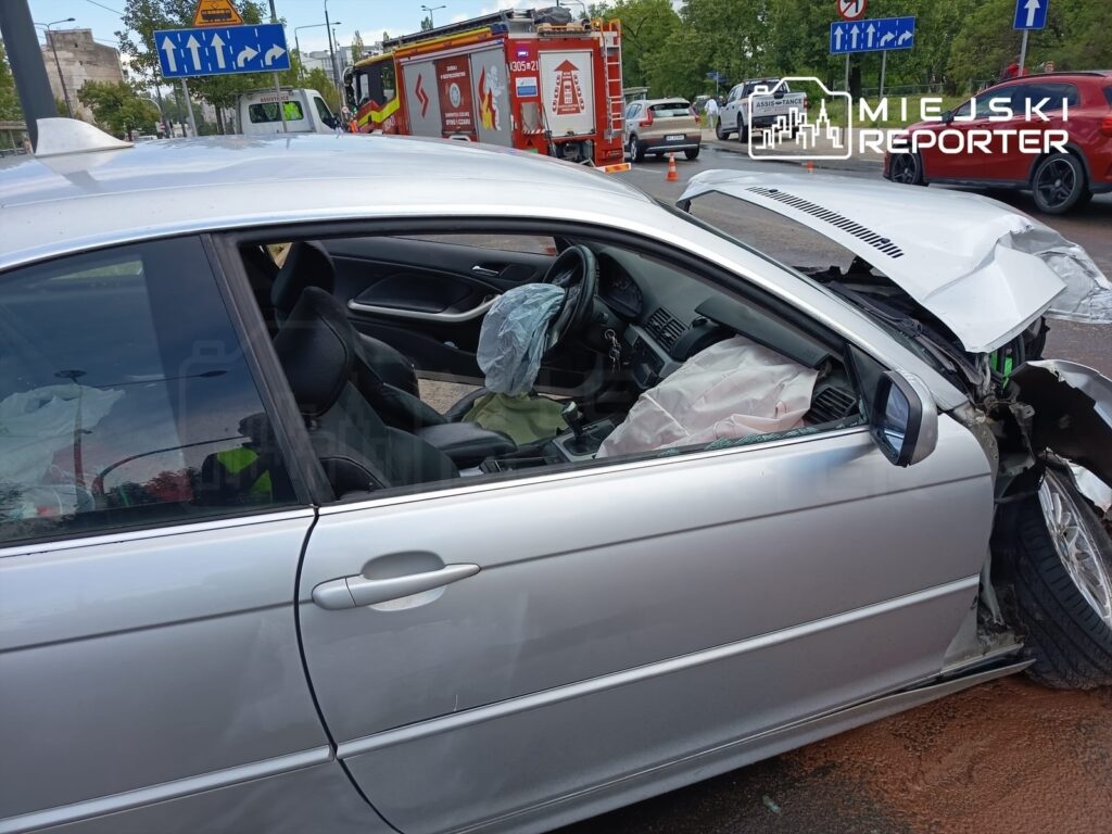 Uszkodzony samochód osobowy z wgniecioną karoserią i poduszką powietrzną włączoną, zaparkowany na ulicy.