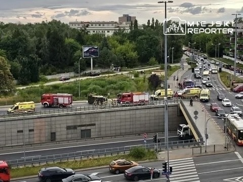 Zespół służb ratunkowych z wozami strażackimi i ambulansami blokuje ruch na drodze przy wjeździe do tunelu.