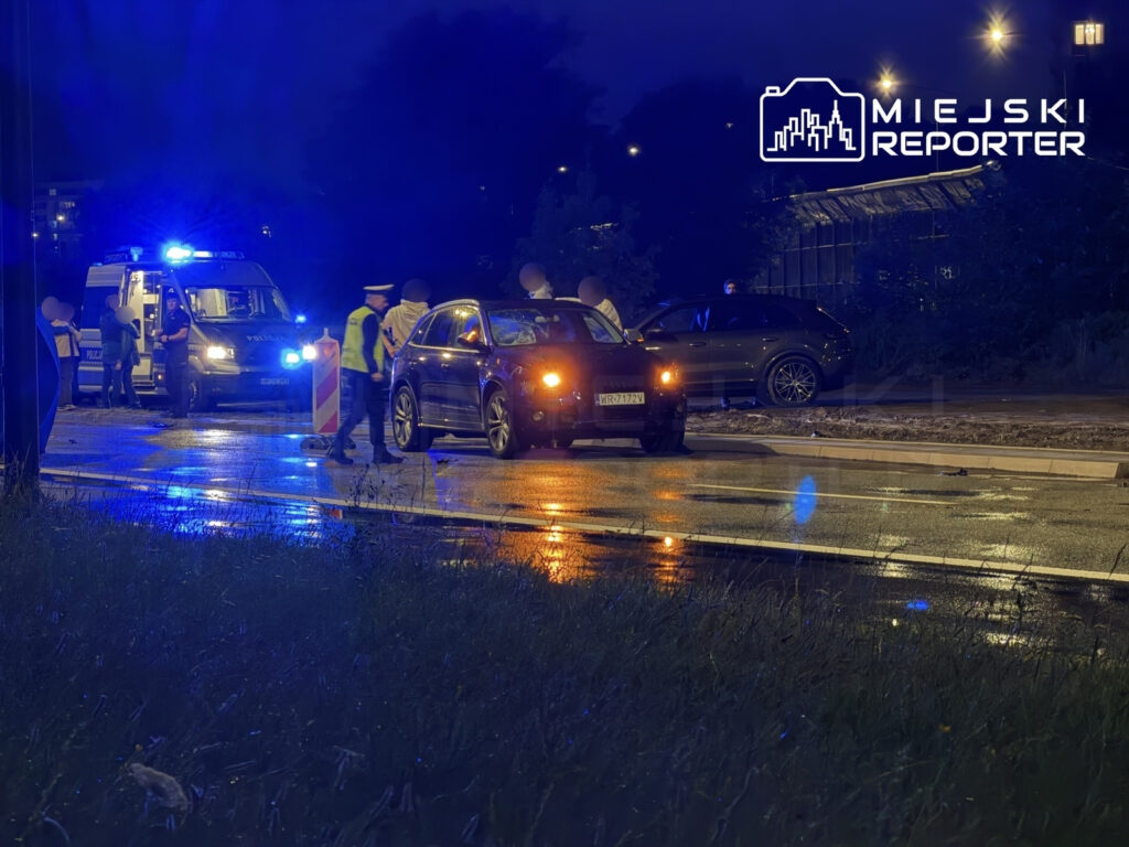 Policjant kontrolujący kierowcę w samochodzie osobowym podczas nocnej akcji na mokrej ulicy. W tle widać radiowóz.