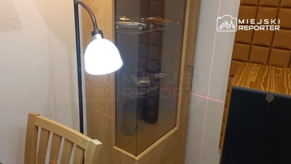 Szafka z przeszklonymi drzwiami, w której znajdują się modele samochodów, oświetlona lampą stojącą.