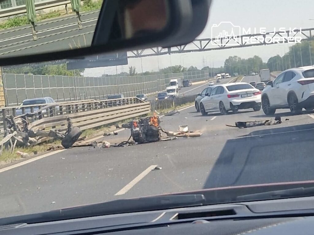 Na jezdni leżą fragmenty pojazdu oraz odzież, a w tle widać ruch samochodów na autostradzie.