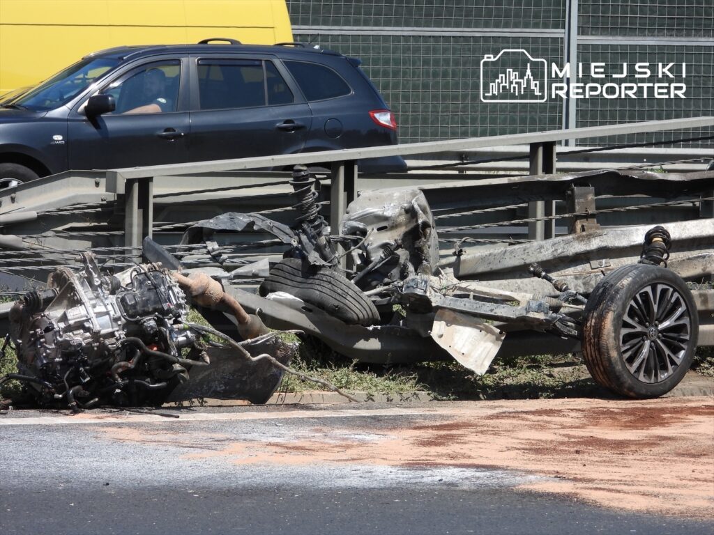 Na jezdni leży uszkodzony silnik i fragmenty zawieszenia samochodu, obok widoczna jest opona oraz plama oleju.