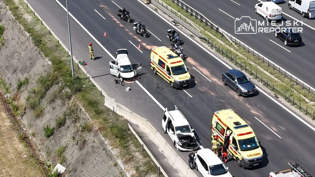 Na drodze ekspresowej zatrzymane pojazdy po wypadku, obok ambulans i strażacy, w tle przejeżdżające samochody.