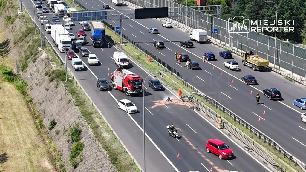 Na drodze ekspresowej S8, samochody stoją w korku obok miejsca wypadku, gdzie strażacy usuwają silnik i koła Toyoty.