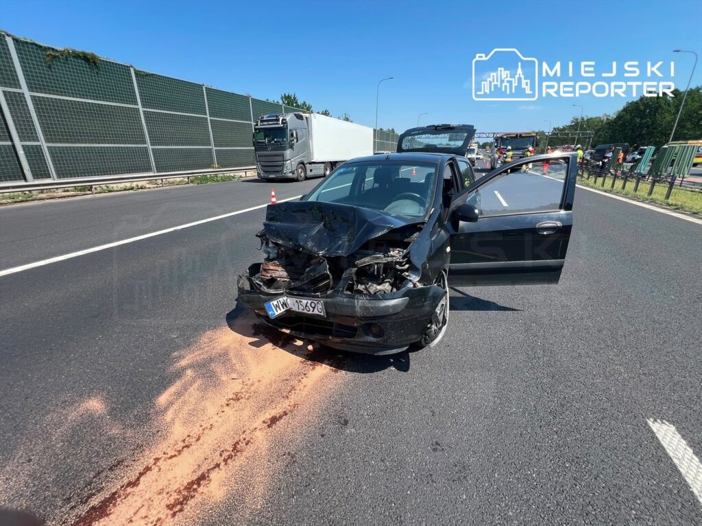 Czarny samochód osobowy z uszkodzoną przednią częścią stoi na pasie ruchu, obok widoczna jest ślad z płynów.