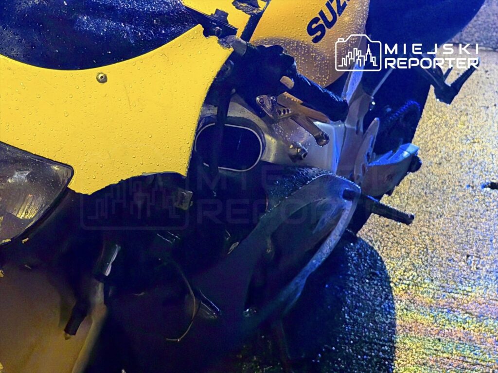 Zniszczony motocykl w kolorze żółtym z mokrą powierzchnią, stojący na asfalcie po deszczu.