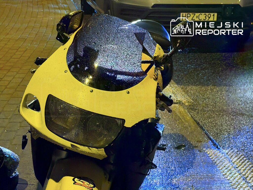 Żółty motocykl z kroplami deszczu stojący na mokrej nawierzchni, obok zaparkowane samochody.