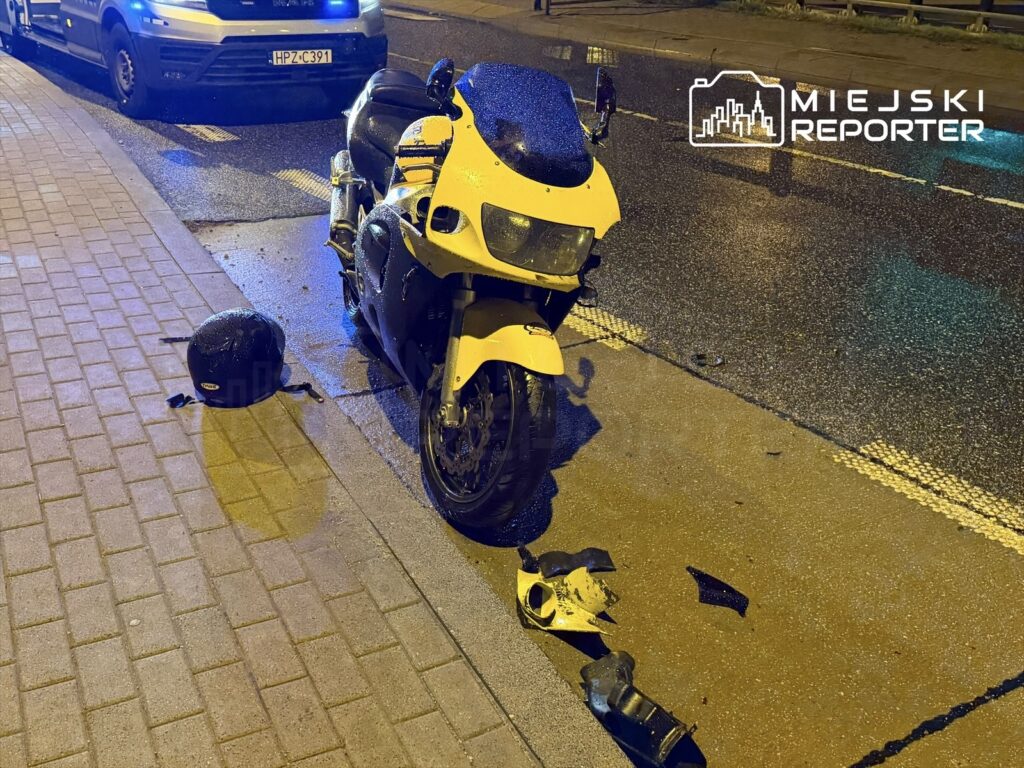 Złamany motocykl w jaskrawym żółtym kolorze stoi na mokrej jezdni obok leżącego kasku i fragmentów odzieży.