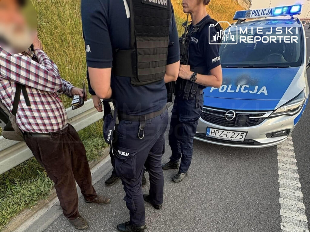 Mężczyzna w koszuli w kratę rozmawia z policjantami obok radiowozu na ekspresówce.