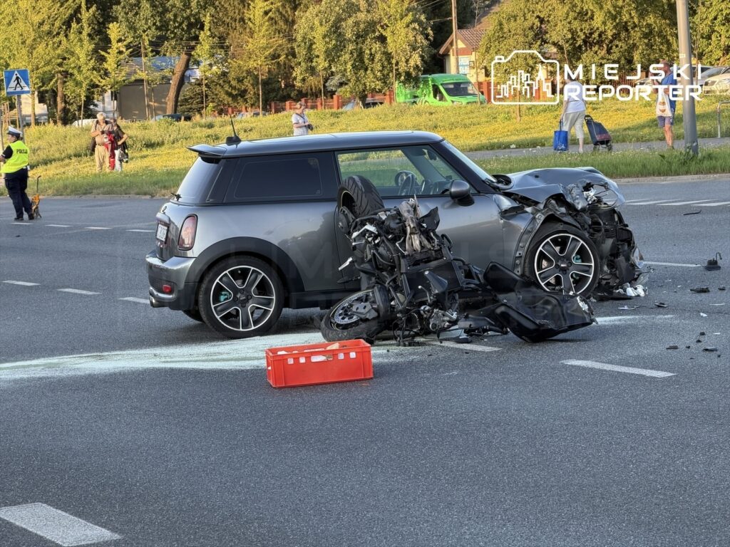 Motocykl zniszczony po zderzeniu z samochodem osobowym na ruchliwej drodze, obok stojący funkcjonariusz policji.