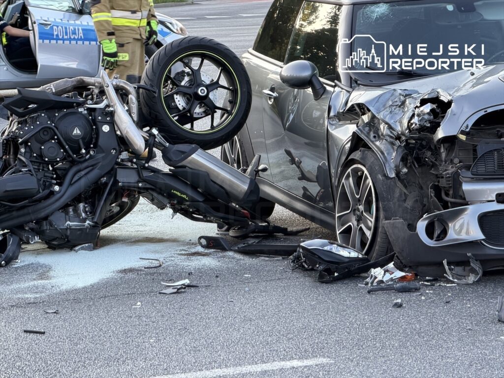 Motocykl leży na boku obok uszkodzonego samochodu Mini, w tle widać radiowóz policyjny.