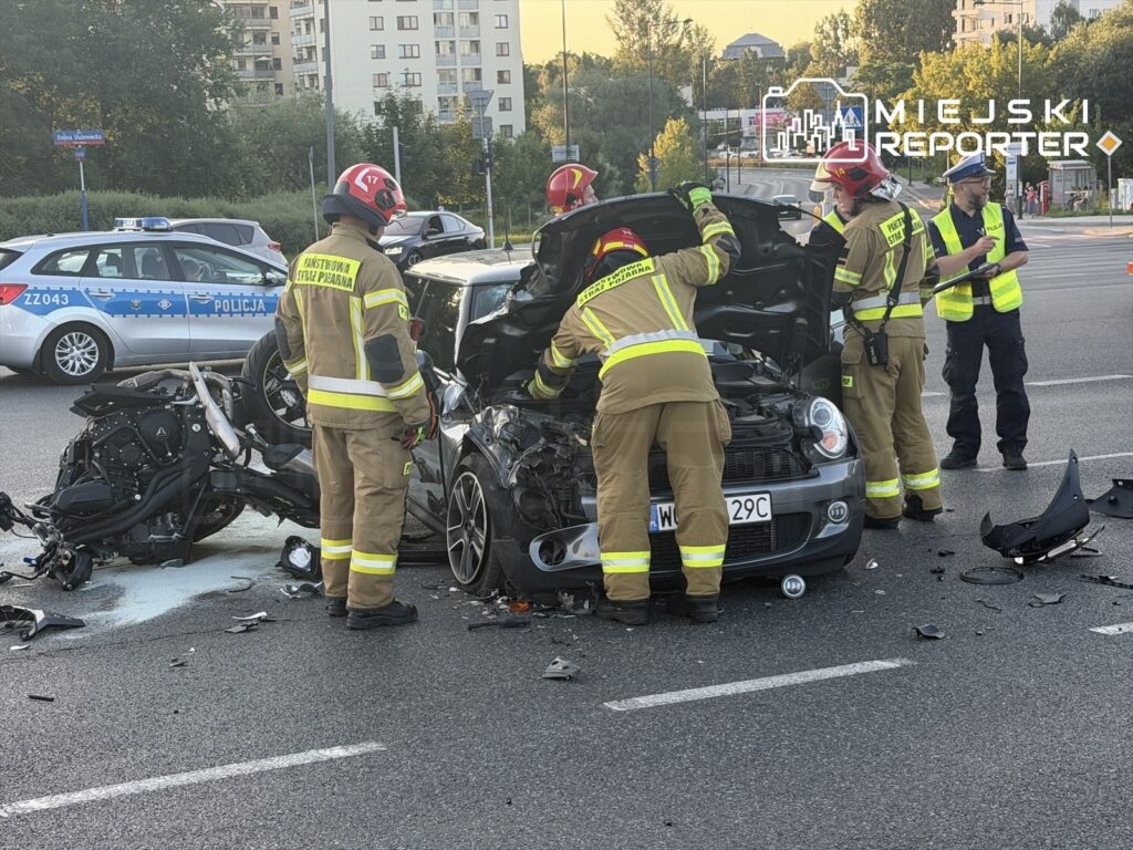 Strażacy pracują nad rozbitym samochodem osobowym po wypadku z motocyklem na ruchliwej ulicy.