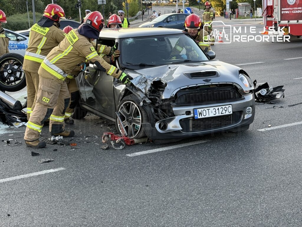 Strażacy w mundurach pracują nad usunięciem uszkodzonego samochodu osobowego po wypadku drogowym.
