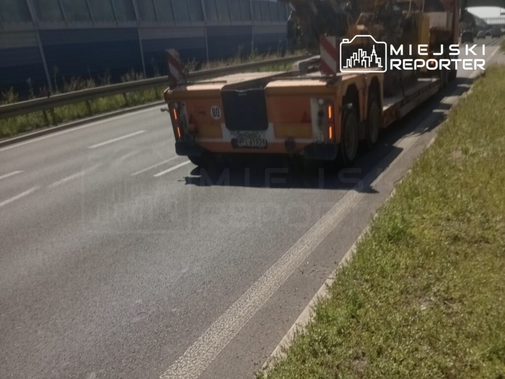Ciężarówka z widocznym oznaczeniem stoi na poboczu drogi ekspresowej, obok pasów ruchu.
