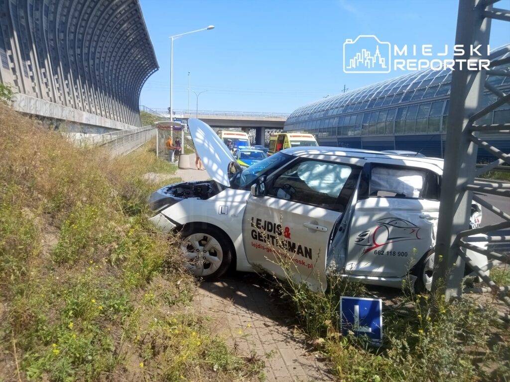 Zniszczony samochód nauki jazdy stał zaparkowany na poboczu, z otwartą maską, obok ruchliwej drogi.