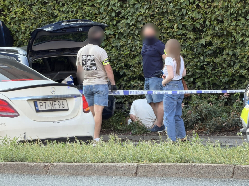 Policjanci rozmawiają z osobami na miejscu zdarzenia, obok białego samochodu z otwartym bagażnikiem.