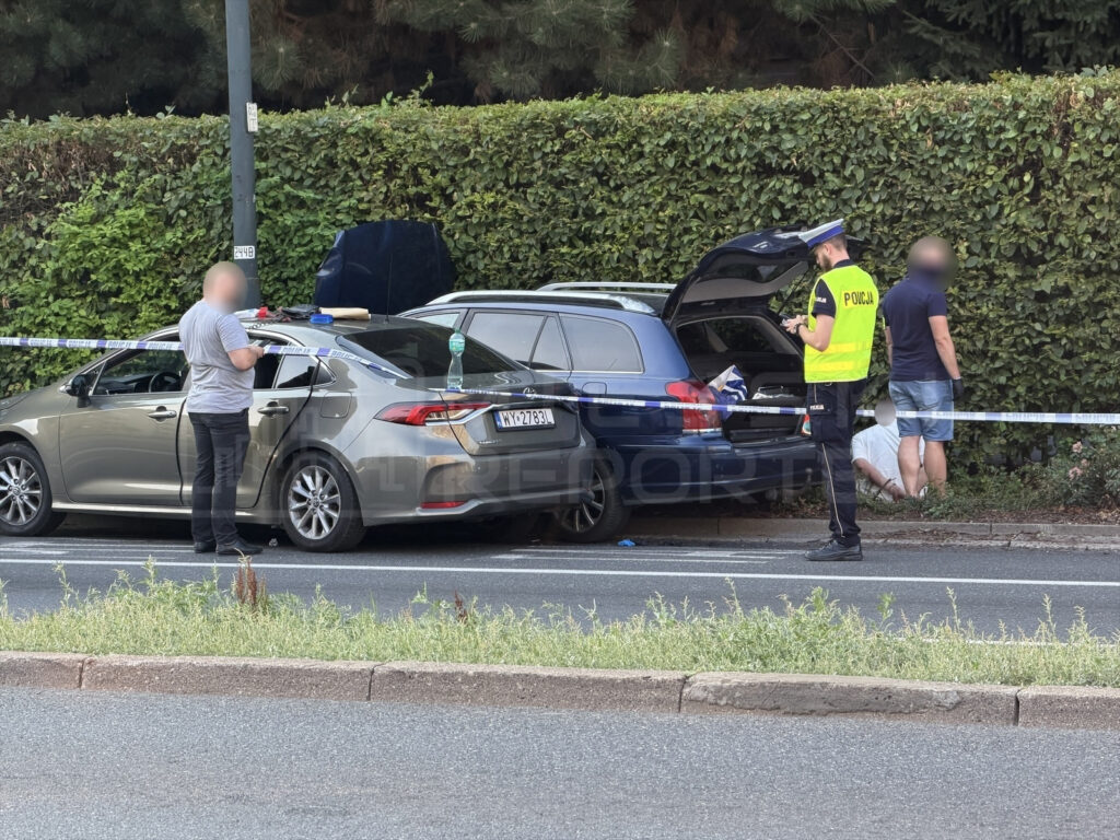 Policjant w kamizelce odblaskowej prowadzi dochodzenie przy dwóch samochodach, otoczonych taśmą policyjną.