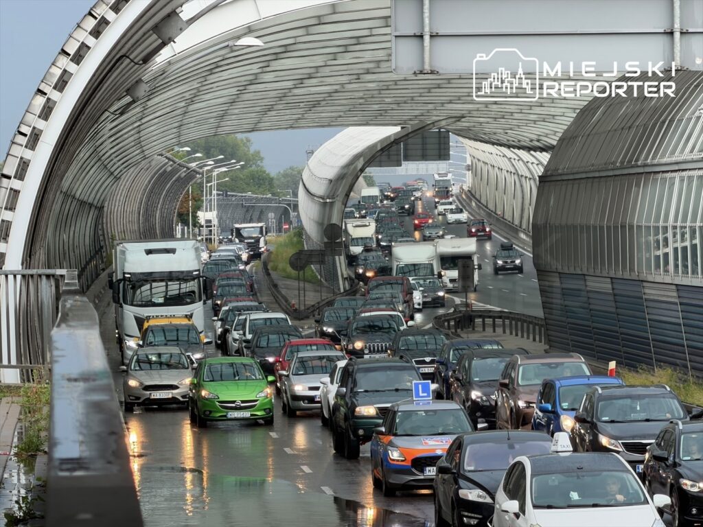Ruch samochodowy wzdłuż zadaszonej trasy, z samochodami stojącymi w korku na mokrej nawierzchni.
