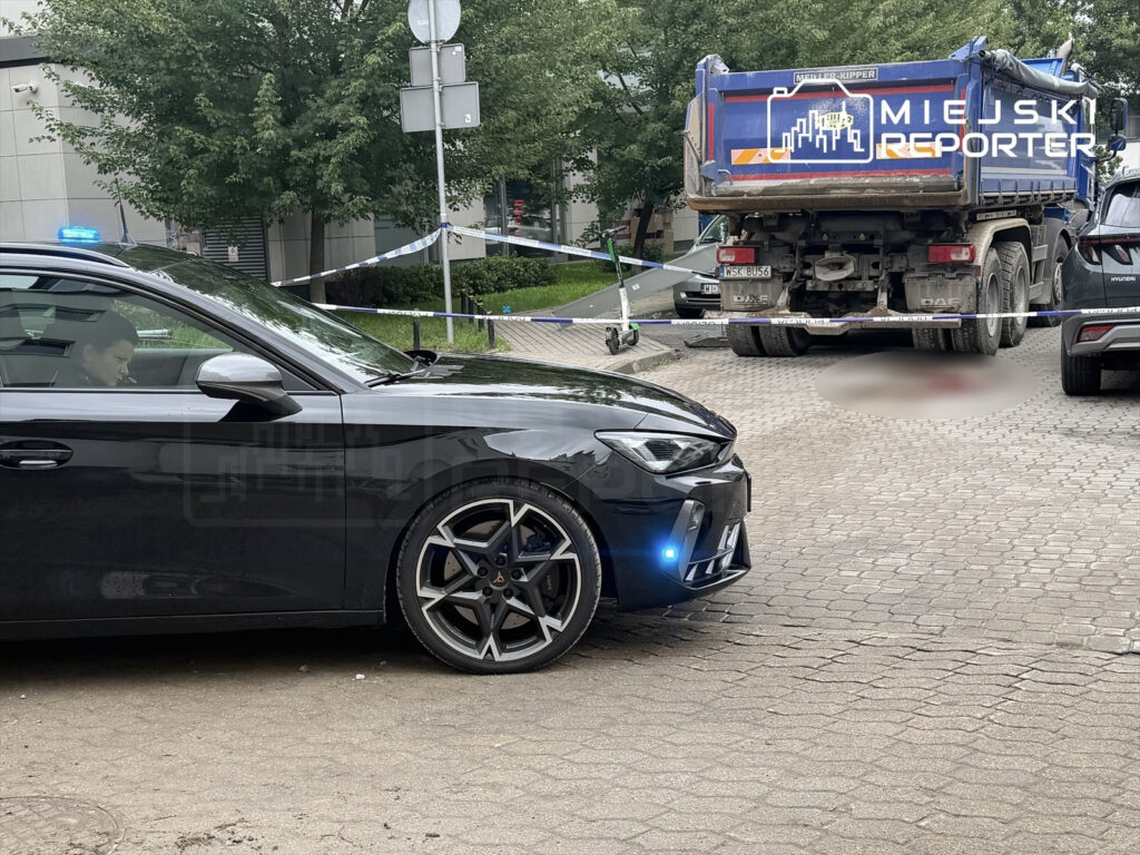 Czarny samochód osobowy z niebieskimi światłami stoi obok ciężarówki na drodze, otoczonej taśmą policyjną.