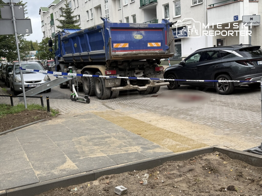 Ciężarówka blokująca ulicę z policyjną taśmą zabezpieczającą, obok leżący skuter i zaparkowane samochody.