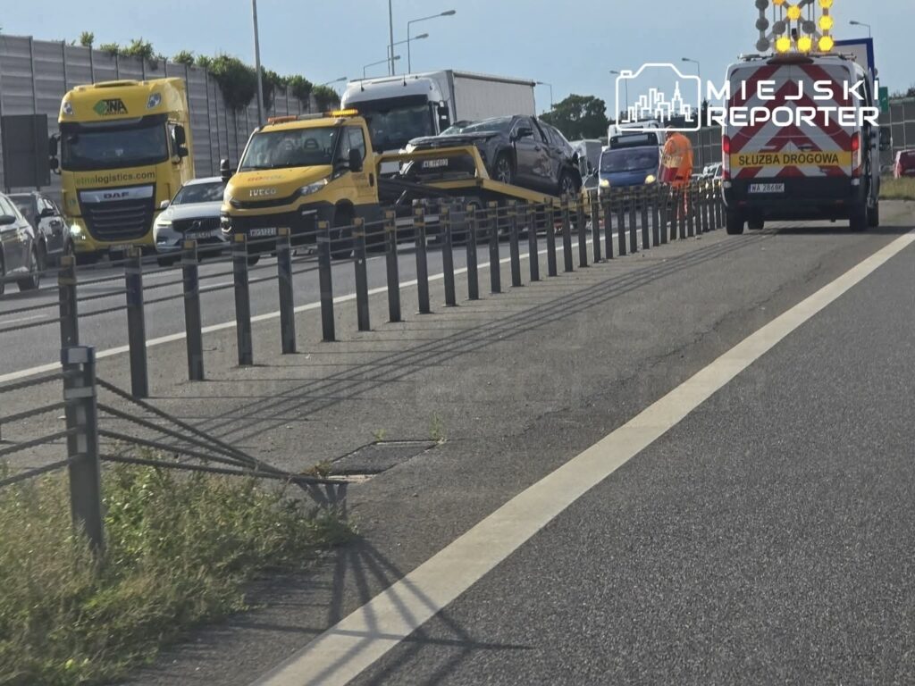 Na drodze widoczna stłuczka, z lawetą podnoszącą dachującą toyotę, obok stoją samochody oraz służby drogowe.