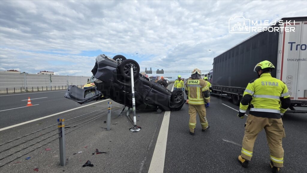 Toyota dachująca na autostradzie, obok strażacy w mundurach, analizujący sytuację.