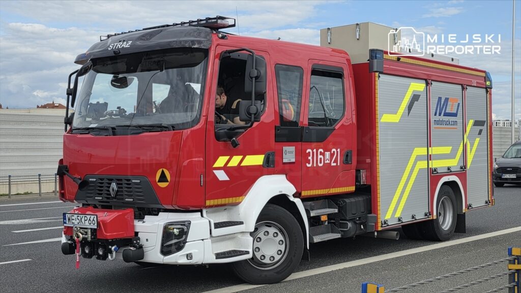 Czerwony wóz strażacki Renault z numerem 316W21 stoi na pasie drogi, a kierowca obserwuje otoczenie.