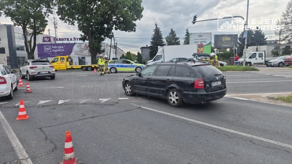Czarny samochód osobowy stoi na drodze, obok grupy ratowników i policjantów w kamizelkach odblaskowych.