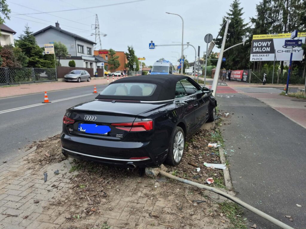 Czarny kabriolet Audi A5 zaparkowany na poboczu, obok leżące fragmenty szkła i uszkodzony słup drogowy.