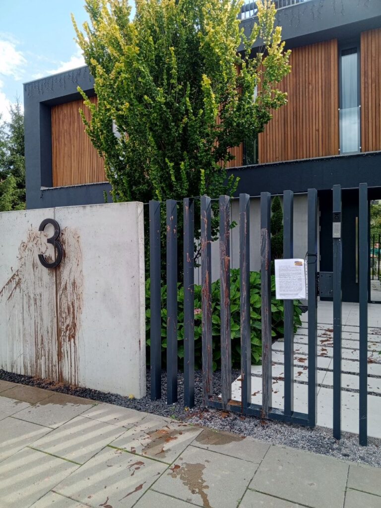 Nowoczesny budynek z drewnianą elewacją, z bramą w stylu minimalistycznym, z widocznymi plamami na betonowym murze.