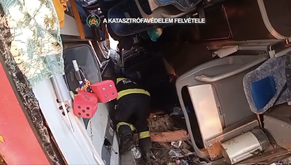 Strażak w mundurze przeszukuje zniszczony autobus, w którym leżą porozrzucane siedzenia i odpady.