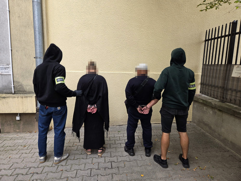 Czterech policjantów zatrzymuje dwie osoby z rękami związanymi za plecami w miejskim otoczeniu.