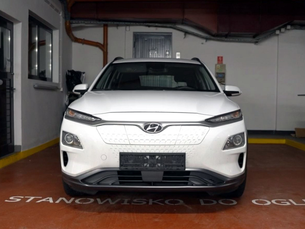 Biały samochód marki Hyundai zaparkowany w zamkniętym pomieszczeniu, z widocznym napisem „STANOWISKO DO OGLĄDU” na podłodze.