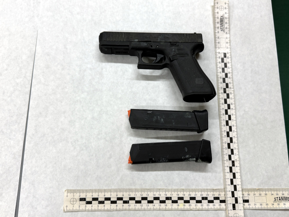 Pistolet półautomatyczny z dwoma magazynkami leży na białym tle, obok linijki do pomiaru.