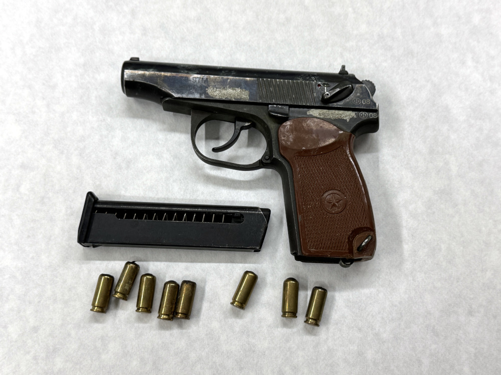 Pistolet z brązową rękojeścią leży obok magazynka i kilku łusek na białym tle.