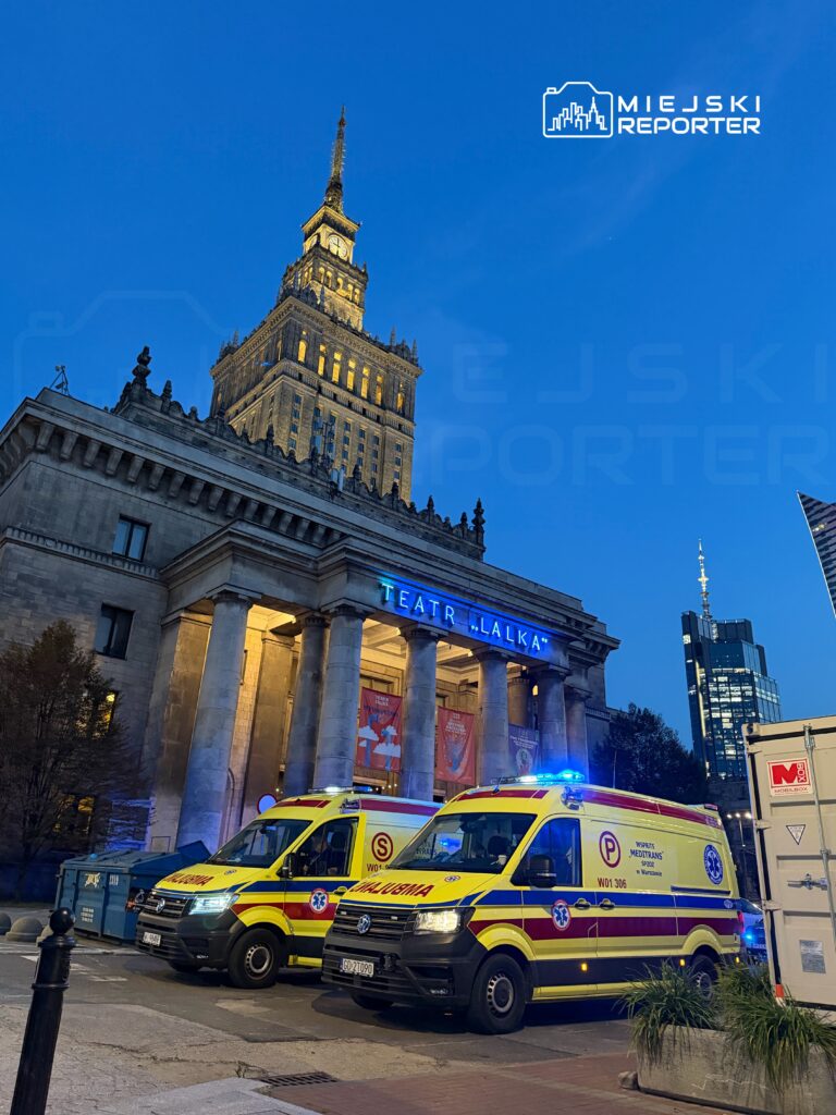 Ambulansy z włączonymi syrenami stoją przed Teatrem Lalek, w tle widoczny oświetlony Pałac Kultury i Nauki.