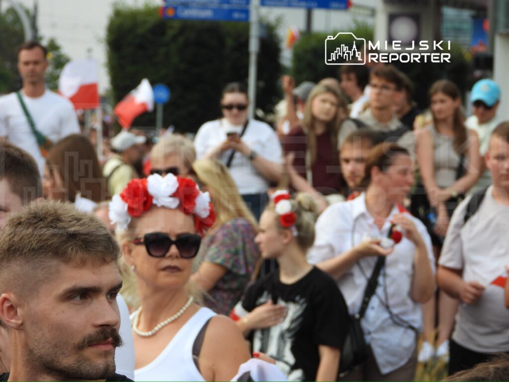 Grupa ludzi w różnorodnych strojach, część z nich z flagami, uczestniczy w wydarzeniu na ulicy.
