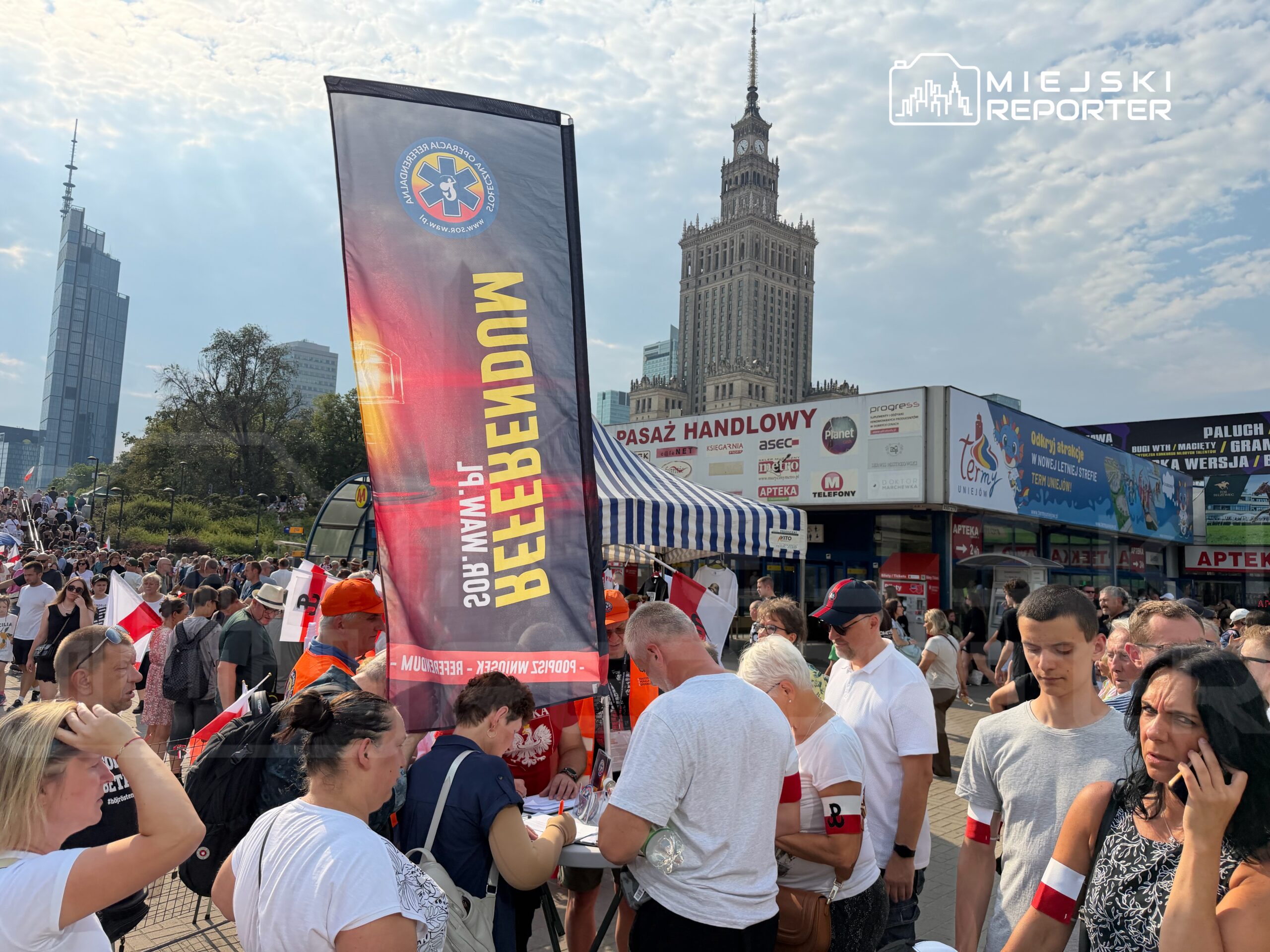 Tłum ludzi z flagami narodowymi w tle nowoczesnych budynków, w tym Pałacu Kultury i Nauki, podczas wydarzenia.