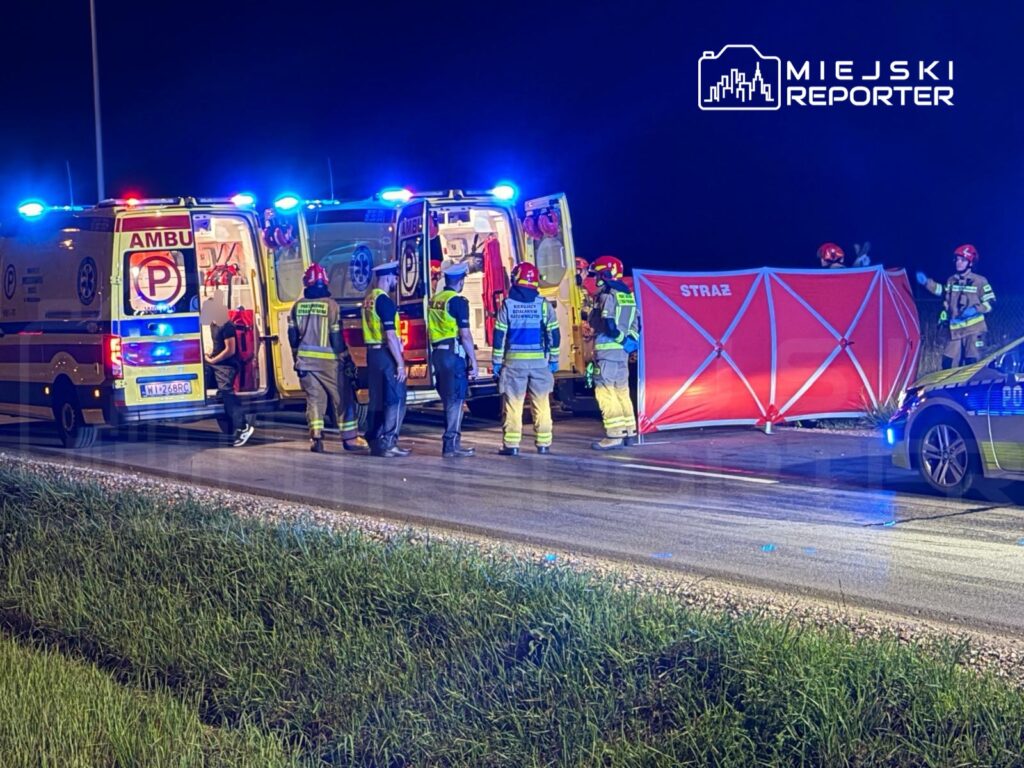 Zespół ratowników medycznych i strażaków pracuje na miejscu wypadku, obok dwóch ambulansów i policyjnego radiowozu.