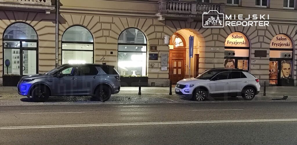 Dwa samochody zaparkowane na ulicy przed budynkiem z dużymi oknami i neonowymi napisami "Salon Fryzjerski".