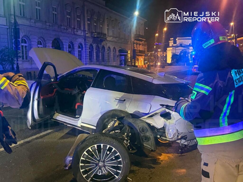 Ratownicy w odblaskowych strojach badają uszkodzone auto po wypadku na oświetlonej ulicy.